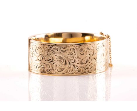 A 9ct yellow gold hinged bangle, the hollow bracelet is engraved with scrollwork design, completed with tongue and groove cla