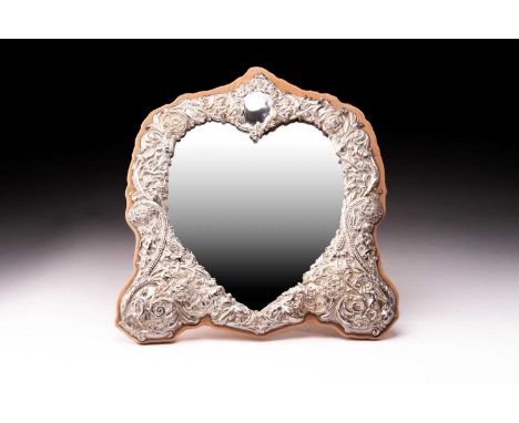 A heart-shaped silver frame dressing table mirror; in late 19th-century taste and chased with putti, scrolls and foliage thro