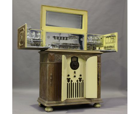 An early 20th century American walnut drinks cabinet radiogram, the hinged top and front enclosing a part set of silvered gla