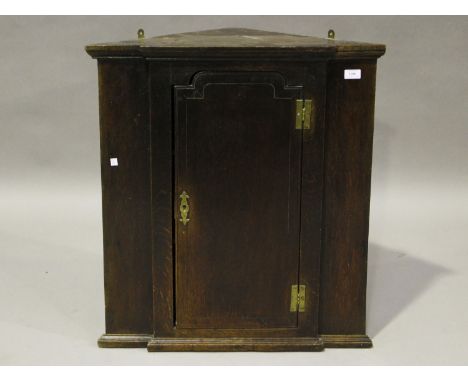 A small George III provincial oak breakfront hanging corner cabinet, the arched door with brass butterfly hinges, enclosing t