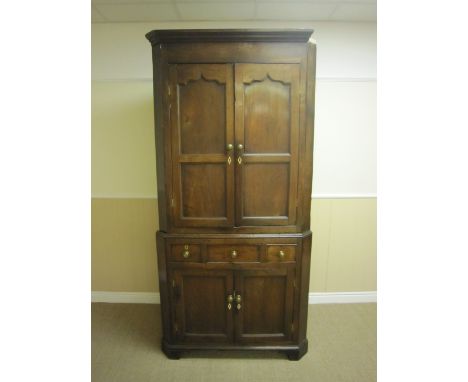 An antique oak double Corner Cupboard having a pair of arched panelled doors enclosing shelves, the base fitted three frieze 