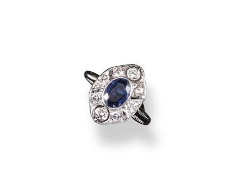 A sapphire and diamond cluster ring, the oval~shaped sapphire is set within a surround of circular cut diamonds and millegrai