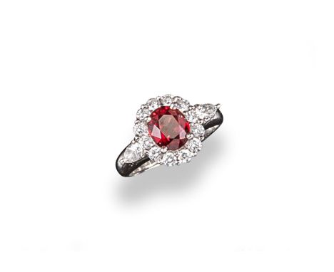 A ruby and diamond cluster ring, the oval~shaped ruby is set within a surround of circular cut diamonds with a further pear~s