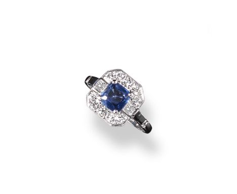 A sapphire and diamond cluster ring, the cushion~shaped sapphire is set within an octagonal surround of circular cut diamonds