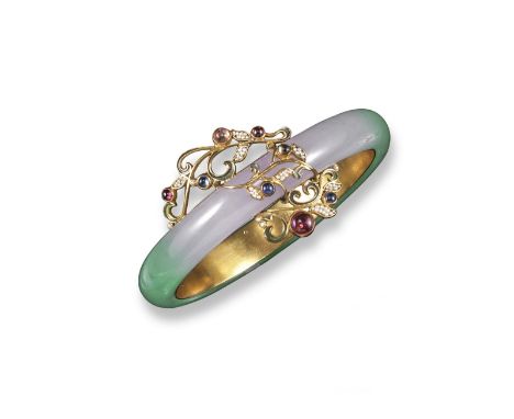 A jadeite bangle, the graduated lavender and green jadeite set in silver~gilt gem set foliate and scrolling mount. 6.3cm inne