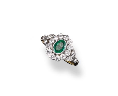 An emerald and diamond cluster ring, the oval~shaped emerald is set within a surround of circular cut diamonds with smaller d