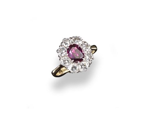 A ruby and diamond cluster ring, the oval~shaped ruby is set within a surround of eight circular cut diamonds in platinum and