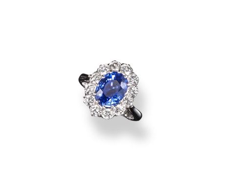 A sapphire and diamond cluster ring, the oval~shaped sapphire is set within a surround of twelve round brilliant cut diamonds