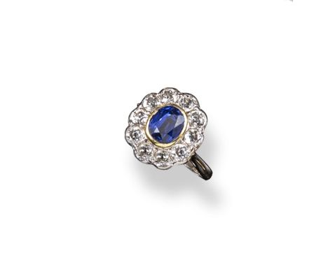 A sapphire and diamond cluster ring, the oval shaped sapphire is set within a surround of ten old circular cut diamonds in wh