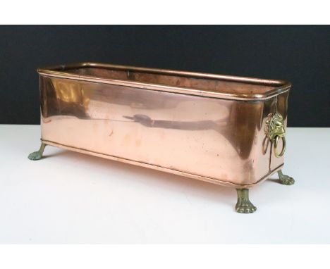 Copper rectangular planter with rolled rim and brass lion mask drop ring handles, raised on brass lion paw feet, 37cm long x 