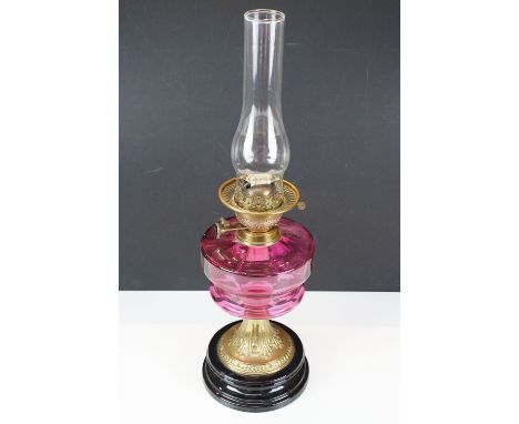 Victorian Cranberry glass oil lamp, glass font and glass chimney. Stood on heavy black ceramic foot with brass base, H 57cm
