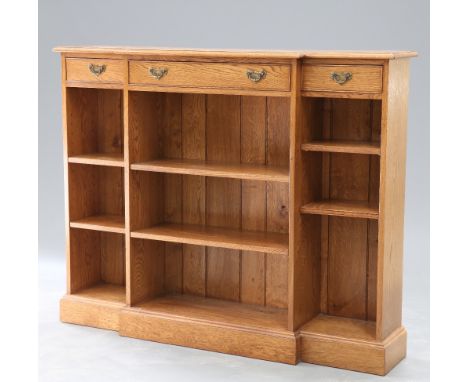 AN EDWARDIAN STYLE LIGHT OAK BREAKFRONT OPEN BOOKCASE, with three drawers over adjustable shelves, raised on a plinth base. 1