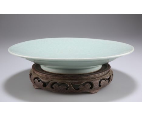 A CHINESE CELADON DISH, circular, carved floral decoration, on a carved and pierced hardwood stand. 28.5cm diameterThe absenc