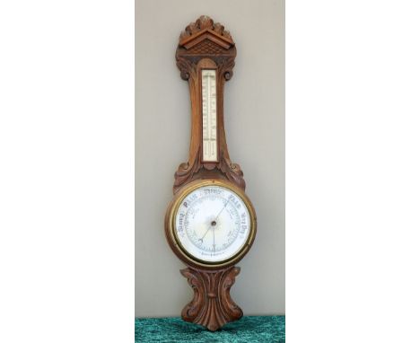 A LATE VICTORIAN OAK ANEROID BAROMETER, the carved oak frame with thermometer and 7 1/2-inch dial. 84.5cm high