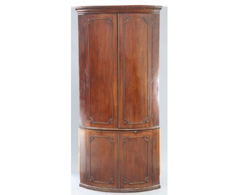 A LARGE GEORGE III MAHOGANY BOW-FRONT DOUBLE CORNER CUPBOARD, the upper section with dentil cornice above a pair of panel doo