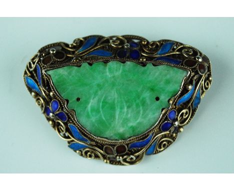 A Chinese jade set brooch, the central carved jade stone set within an enamelled and gilt metal entwined floral surround, sta