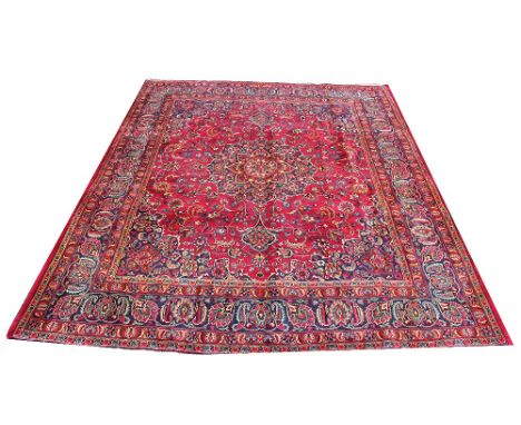 A Persian Heriz wool carpet, worked with a central medallion and all over foliate design against a red ground, with signed ca