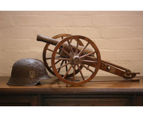 CANNON & HELMET - a model cannon at a length of 73cm and a wheel height of 30cm along with a rusted German military helmet.