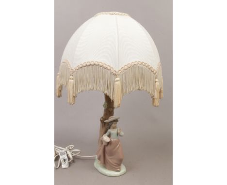 A Nao porcelain figural table lamp, formed as a young girl carrying a basket of flowers with cream fabric shade.