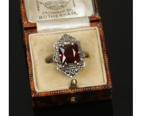 A white metal cocktail ring set with marcasites and a single red stone, size K.