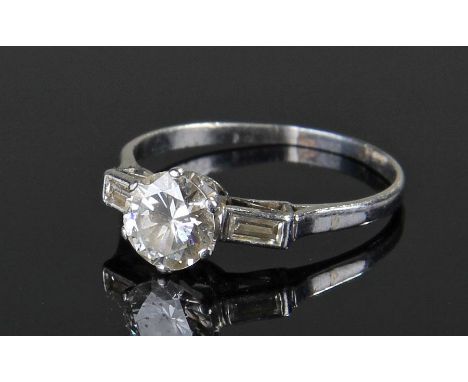White metal and diamond set ring the central approximately 1 carat brilliant cut diamond flanked by a pair of baguette cut di