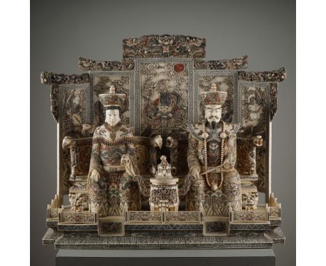 A refined Chinese hand-carved deer bone sculpture depicting an enthroned imperial couple seated against an intricately carved