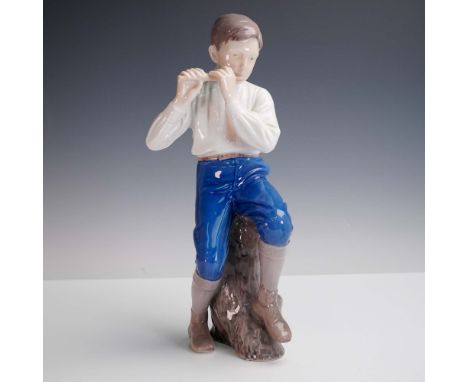 This finely crafted porcelain figurine by Bing &amp; Grondahl of Denmark depicts a young boy playing the flute, seated on a n