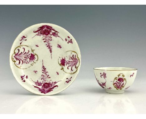 A Worcester tea bowl and sacucer, circa 1765, painted in the Meissen style with puce floral decoration within gilt Rococo car