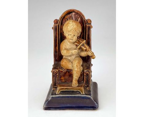 George Tinworth for Doulton Lambeth, a stoneware figural menu holder, modelled as a child playing the fiddle, sitting in a th