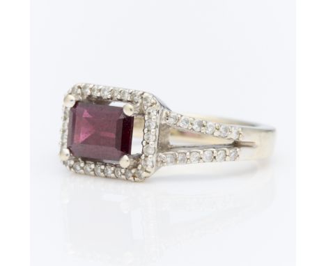 14k white gold ring set with garnets and diamonds. With a central step cut garnet set east west, surrounded by a halo of diam