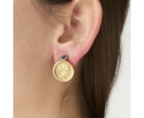A pair of medallion and blue sapphire post earrings. Comprised of a round cut blue sapphire in a bezel setting. Below, a beze