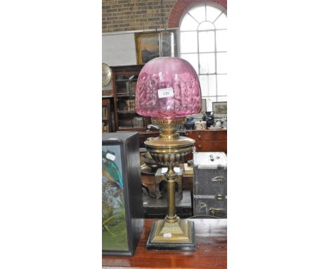 AN EDWARDIAN BRASS OIL LAMP, with a cranberry frosted shade