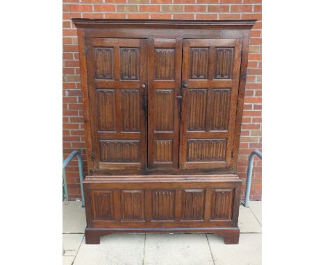 A joined oak press or livery cupboard, 18th century, the ogive cornice above tow linen fold panel cupboard doors enclosing a 