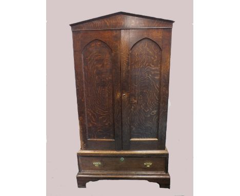 An oak two door cabinet, early 19th century, the architectural pediment above two indented Gothic arch cupboard doors enclosi