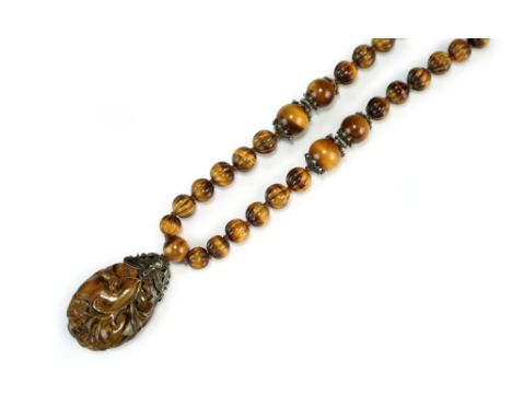 A Chinese tiger's eye and silver pendant necklace, late Qing Dynasty, the pendant of ovoid form and carved as a fruiting peac