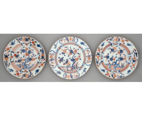 Three Chinese Imari plates, 18th c, painted with a blossoming tree and fence in panelled diaper cavetto, the border sprays di