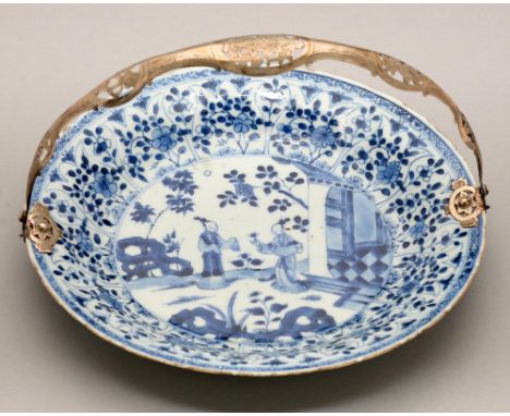 A Chinese blue and white dish, Kangxi period, painted with two figures by a house and hollow rocks, one holding a flower, the