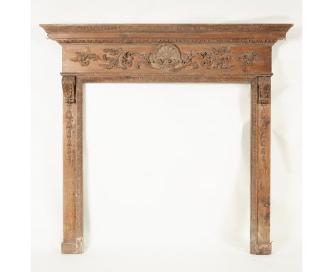 A pine fire surround with shell and scroll carved frieze on bracket supports above trails of harebells, the aperture 102cm x 