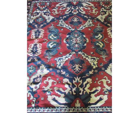 A Turkish woollen carpet decorated with stylized foliate designs in blue and green on a red ground, 260 cm x 230 cm approxima