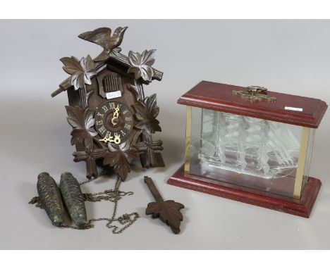 A glass ship in a display case along with a cuckoo clock.