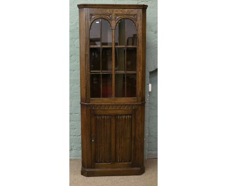 A carved oak astrigal glazed corner cupboard with linen fold patterned doors and arch top display.