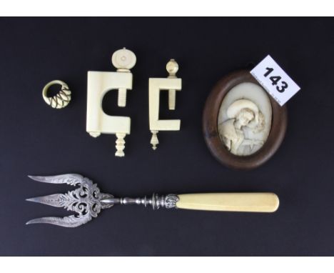 A 19th Century European carved ivory miniature, together with two carved ivory embroidery clamps, an ivory handle bread fork 