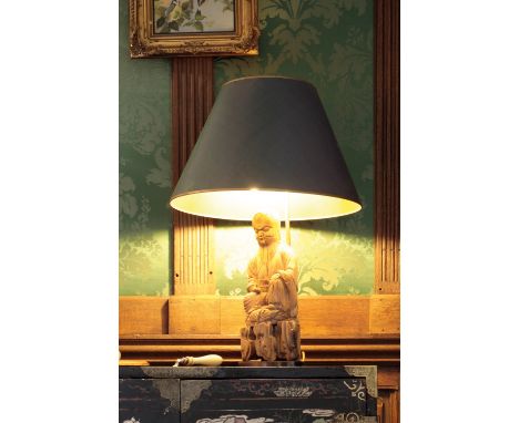 A CARVED WOOD "BUDDHA" TABLE LAMP fitted for electricity and with a green shade, 26.5" high