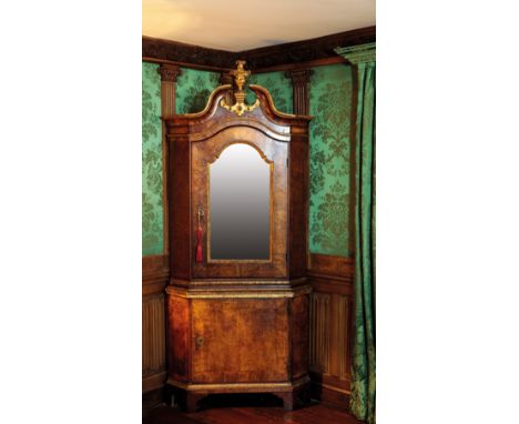 A DANISH WALNUT VENEERED AND PARCEL-GILT STANDING CORNER CUPBOARD, circa 1740, with a moulded swan neck pediment centred by a