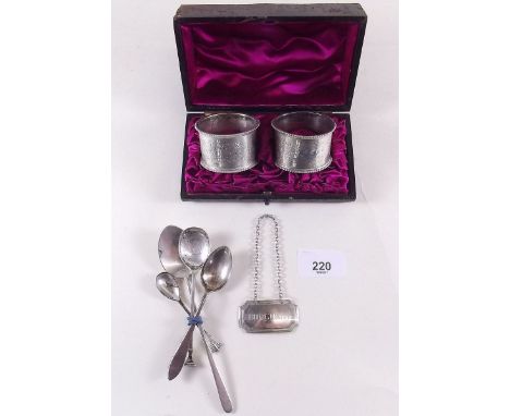 A pair of silver napkin rings cased - 64g, Birmingham 1897, four silver spoons 42g and a brandy decanter label 