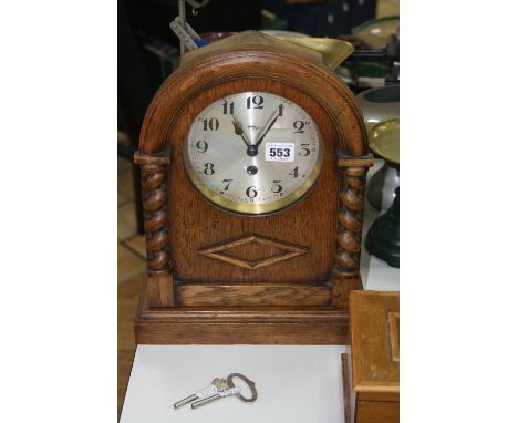 AN OAK MANTLE CLOCK, having dome top over barley-twist supports, silvered dial with Arabic numerals, approximately 36cm high 