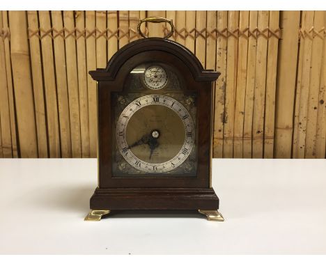ELLIOT MANTEL CLOCK IN WALNUT CASE. BRASS FACE WITH SILVERED CHAPTER RING, ROMAN NUMERALS, CHERUB SPANDRELLS, 8 DAY MOVEMENT,
