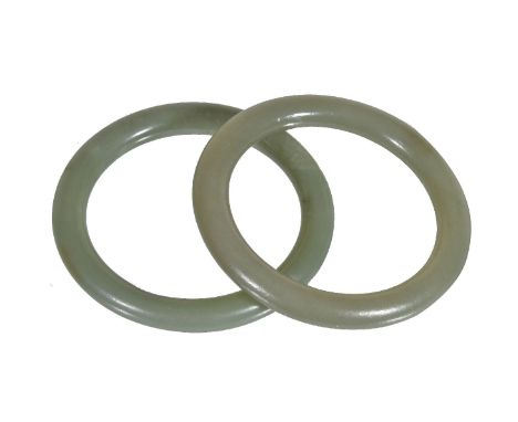 A pair of Chinese green jade bangles, of generally even tone with russet inclusions, 6.9cm diameter and internal diameter 5.2
