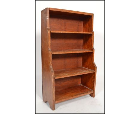 An early 20th century walnut Arts and Crafts inspired waterfall open dwarf bookcase, having four shelves raised on bracket fe