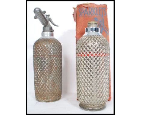 Two vintage oversized Soda Syhons by Sparklets, both with wire mesh covers and one retaining its origonal box